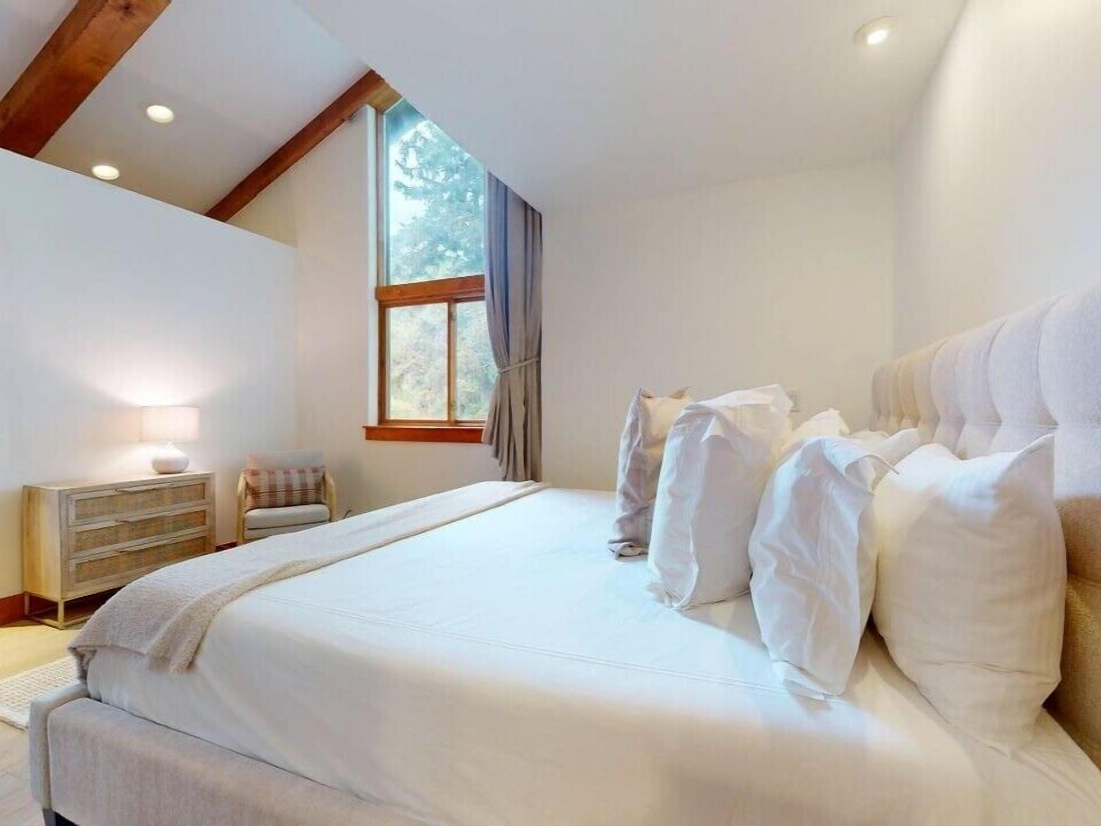 Ein Schlafzimmer mit einem großen Bett, einem Nachttisch, einer Lampe und einem Fenster mit Vorhängen.