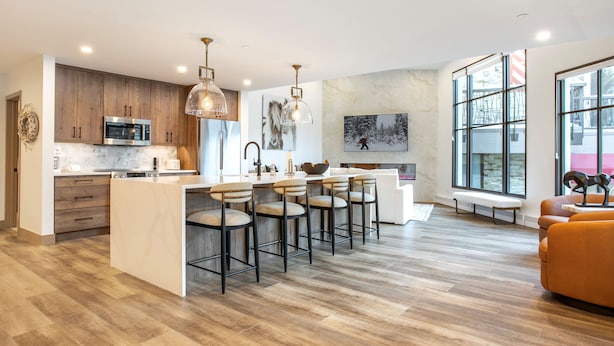 A modern kitchen with a central island, bar stools, and a seating area with a bench and orange sofa. - Christiania Condominiums - Residence Collection (Vail)