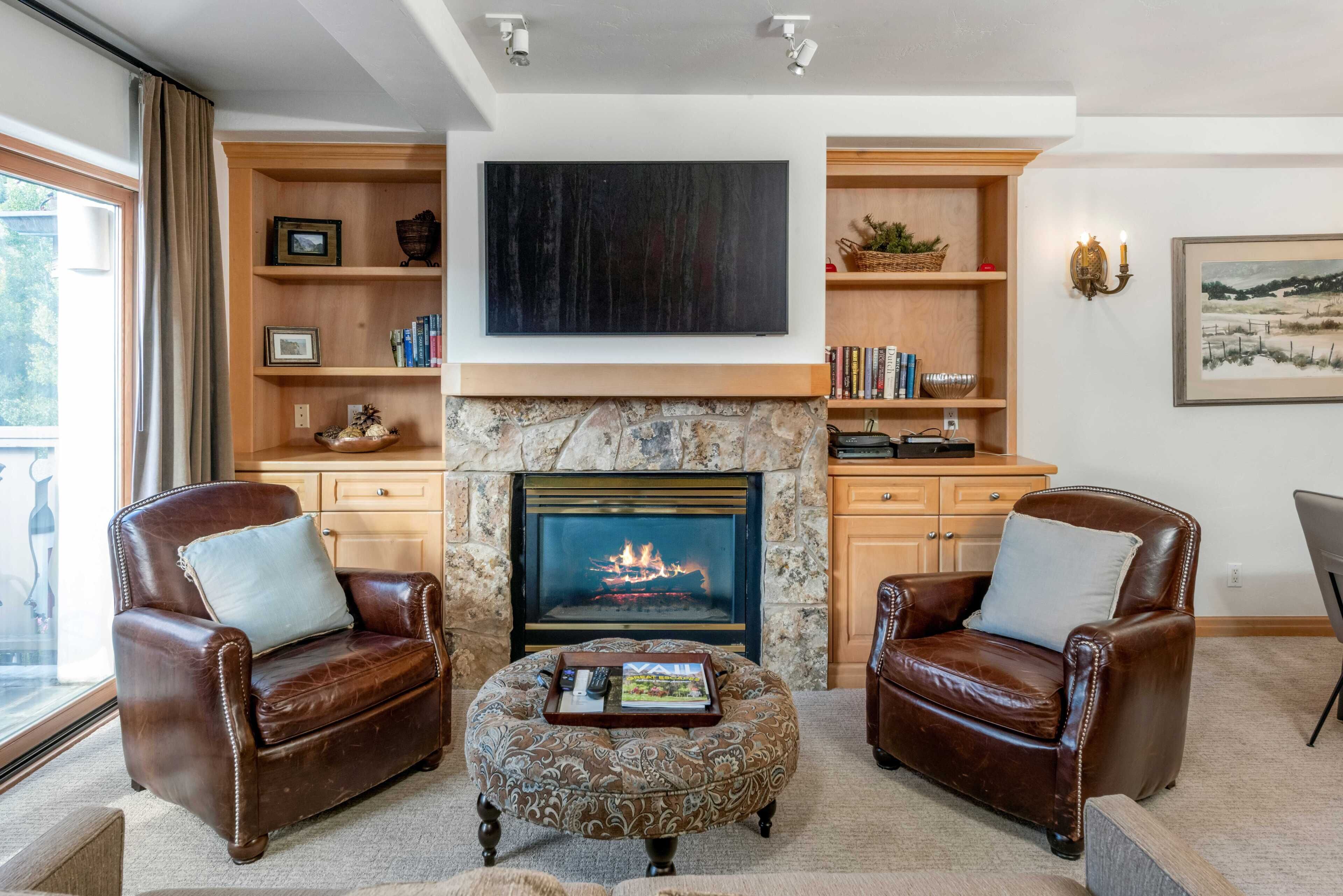 A living room with leather armchairs, a fireplace, a flat-screen TV, and a bookshelf.