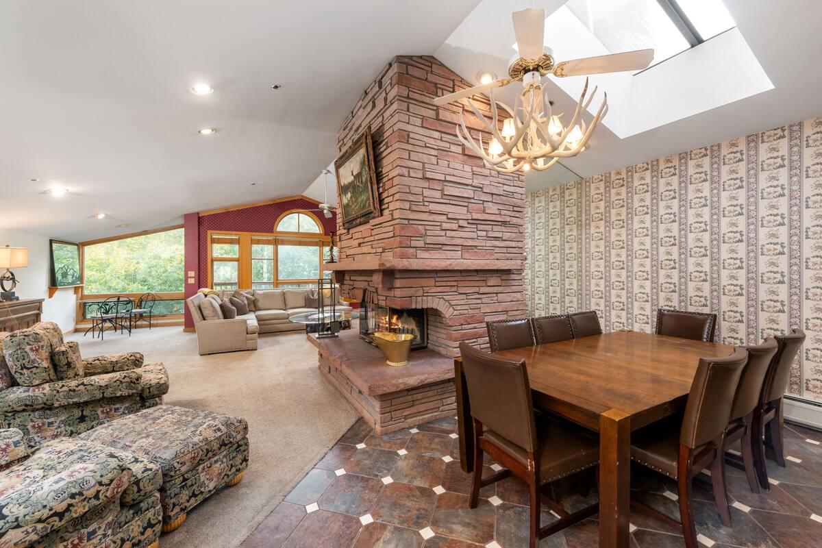 A spacious living room with a fireplace, a dining area with a large wooden table and chairs, and a cozy seating area with patterned sofas.