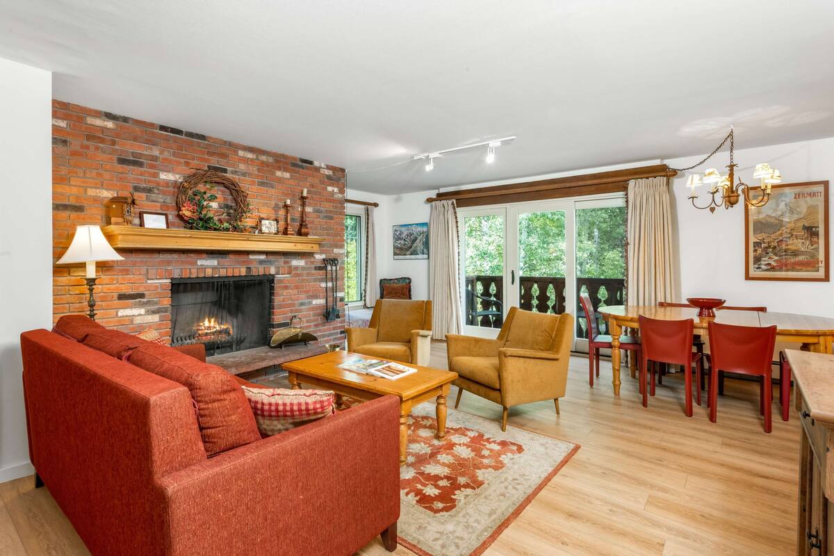 A living room with a brick fireplace, red sofas, a wooden coffee table, and a dining area with a table and chairs.