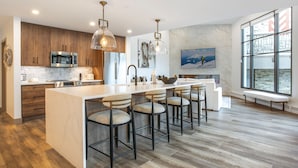 A modern kitchen with wooden cabinets, stainless steel appliances, and a large island with bar stools. - Christiania Condominiums - Residence Collection (Vail)