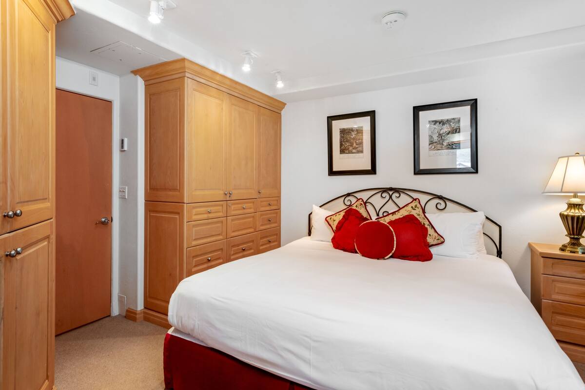 A bedroom with a bed, wooden wardrobe, and two framed pictures on the wall.