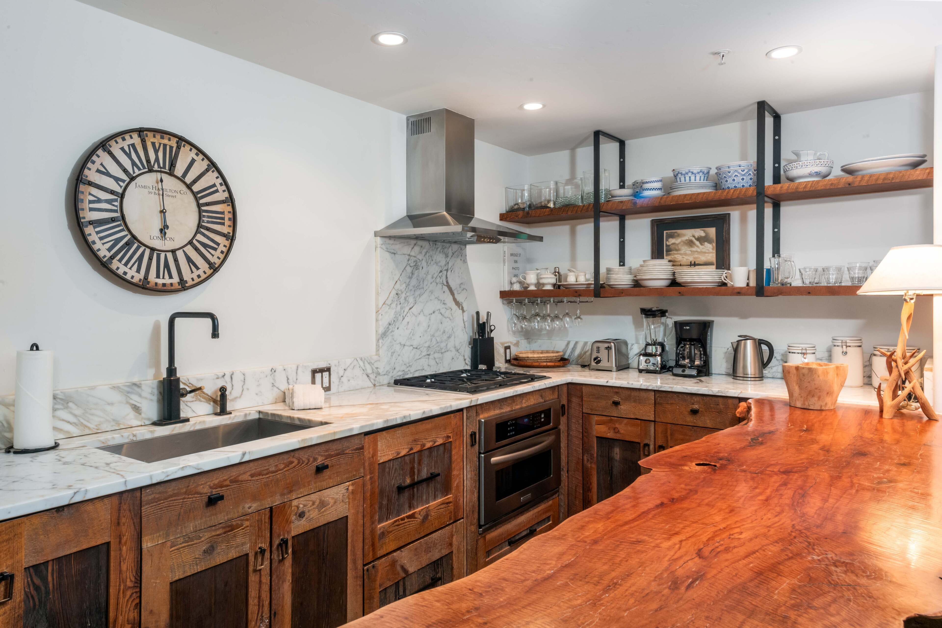 Una cocina moderna con encimera de mármol, armarios de madera, pileta de acero inoxidable y horno integrado.