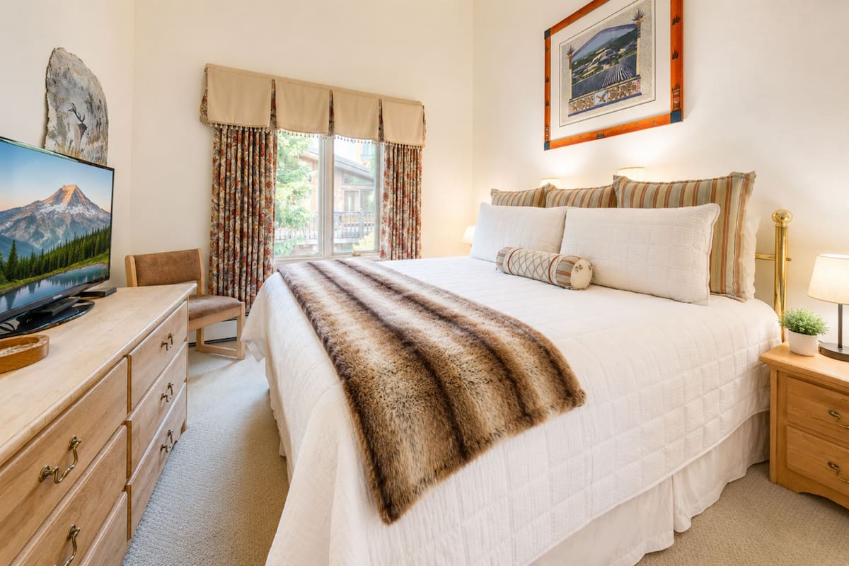 Una camera d'albergo con un letto, una scrivania con televisione, una finestra con tende e un quadro appeso al muro.
