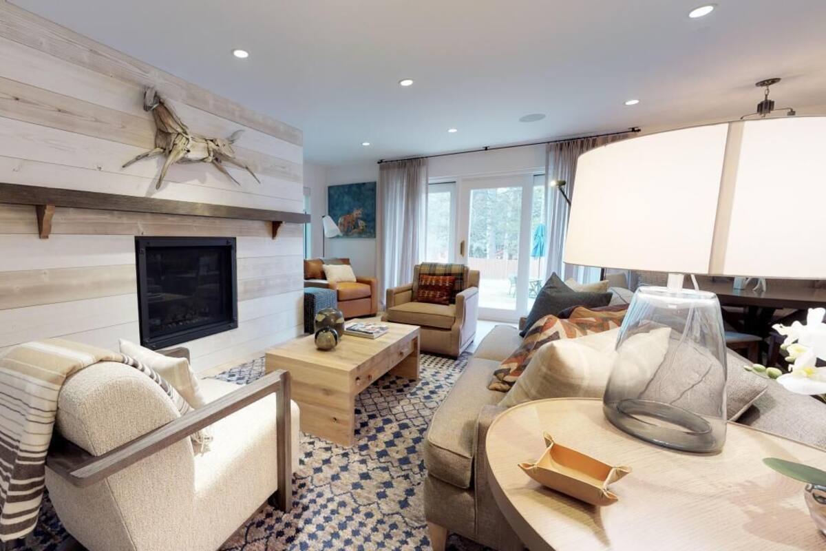 A modern living room with a fireplace, comfortable seating, and a large window.