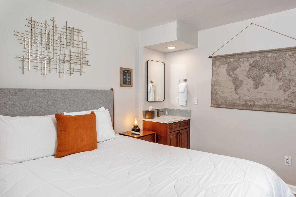 A hotel room with a large bed, a nightstand with a lamp, a bathroom with a sink and mirror, and a world map on the wall.