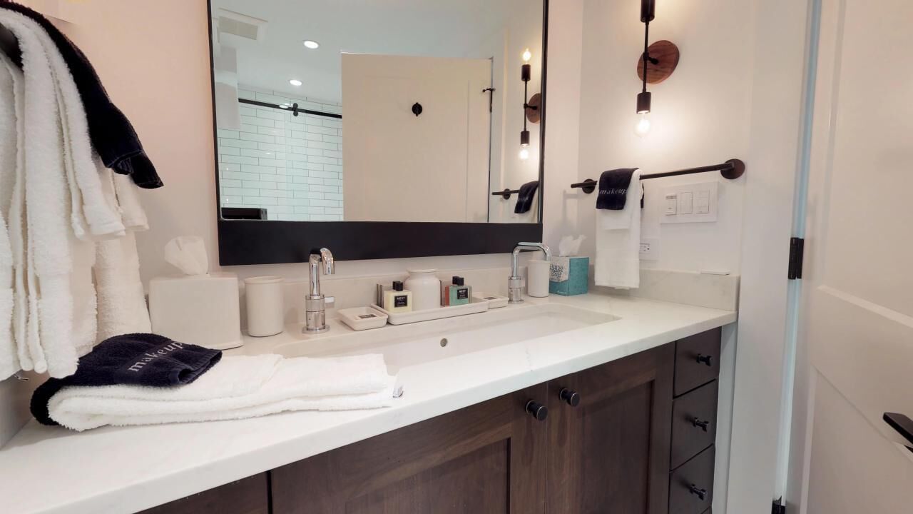 A modern bathroom with a white sink, dark wooden cabinets, a large mirror, and a towel rack with towels.
