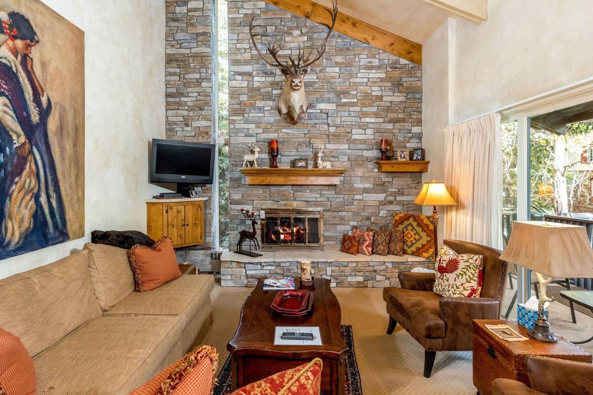 A cozy living room with a stone fireplace, a mounted deer head, and a television.
