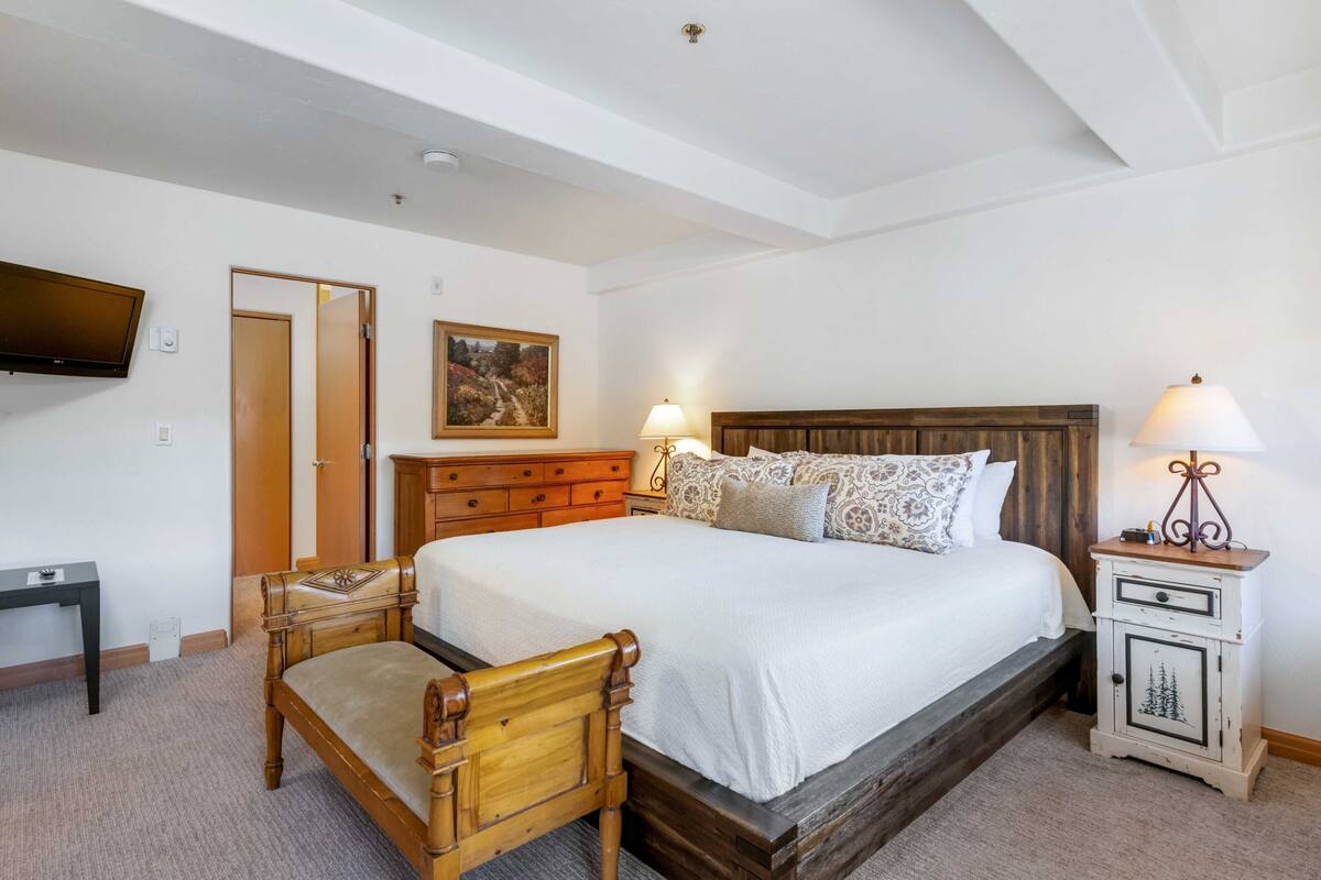 A bedroom with a wooden bed, bedside tables, a TV, and a painting on the wall.