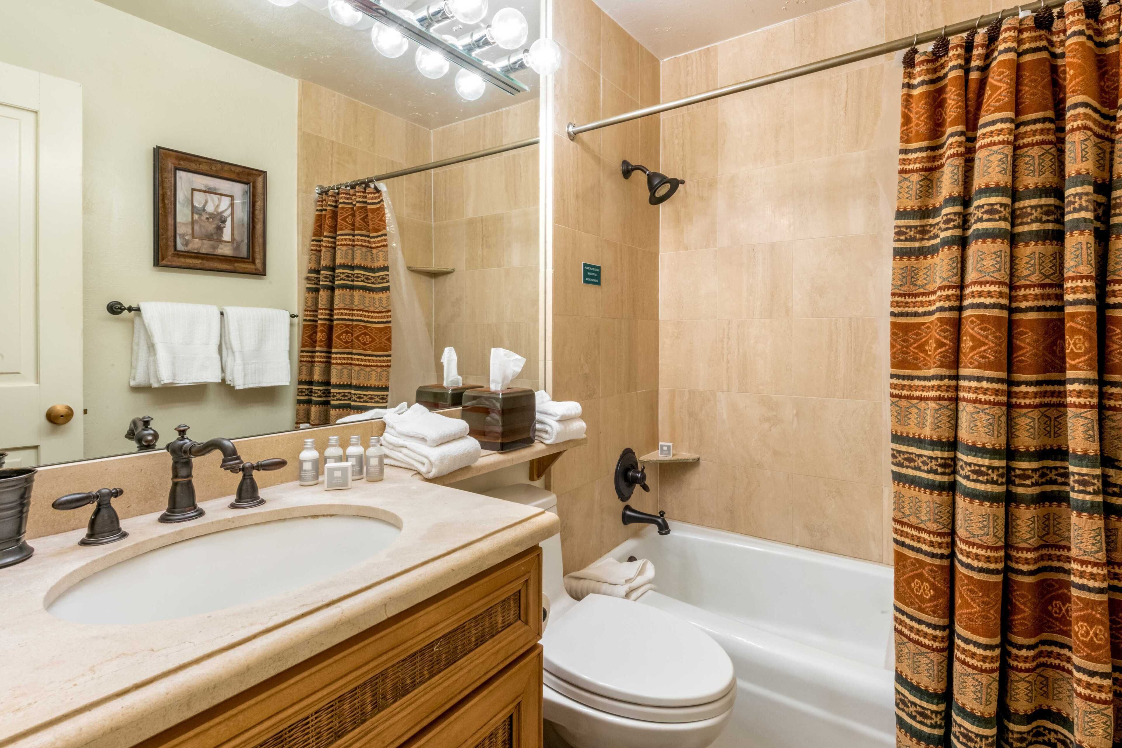 A bathroom with a sink, mirror, towel rack, shower curtain, and a toilet.