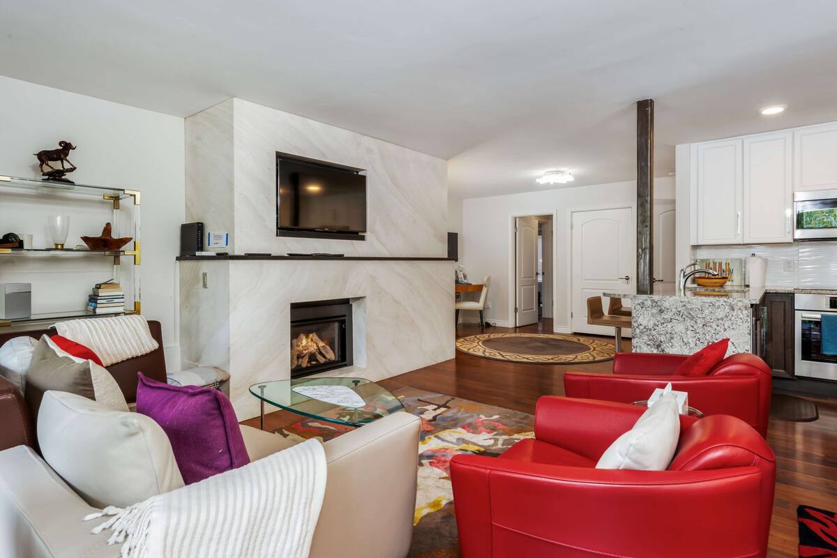 A modern living room with a fireplace, red leather sofas, a glass coffee table, and a flat-screen TV mounted above the fireplace.