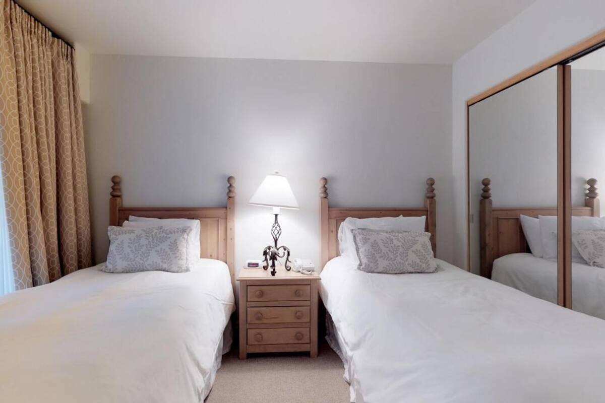 A hotel room with two beds, a nightstand with a lamp, and a large mirror.