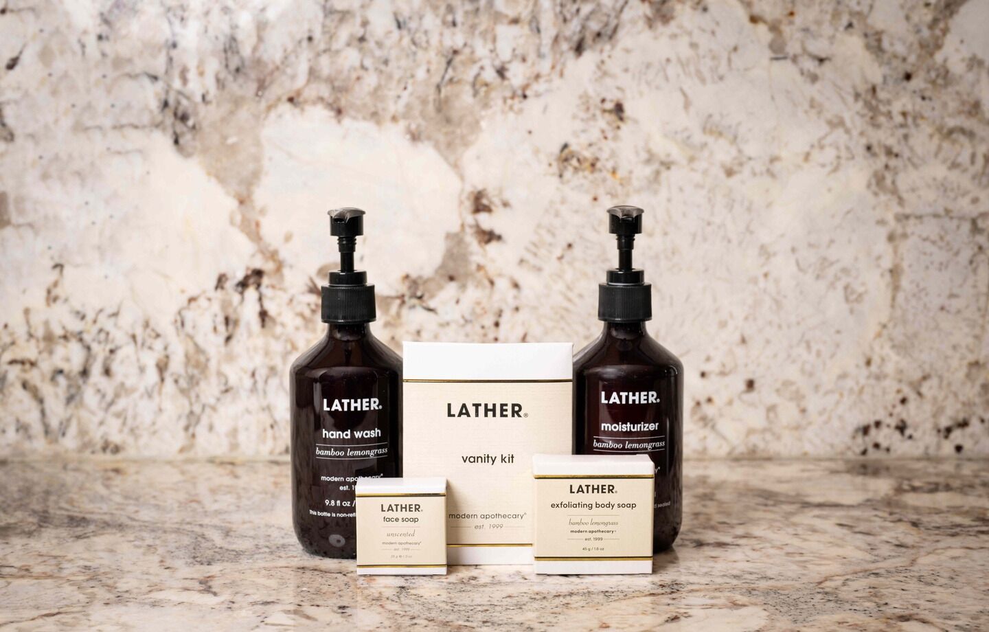 Conjunto de jabón líquido para manos Lather, crema hidratante y jabón exfoliante para el cuerpo, junto con sus empaques, sobre una superficie de mármol.