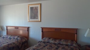Two wooden beds with patterned bedding in a room with a framed picture on the wall.