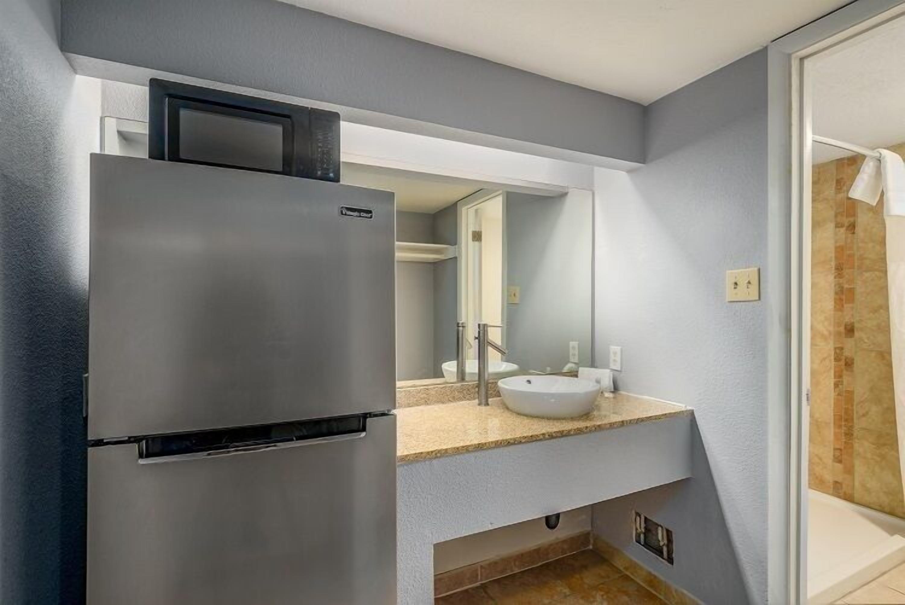 A modern bathroom with a stainless steel refrigerator, a white sink, and a large mirror.