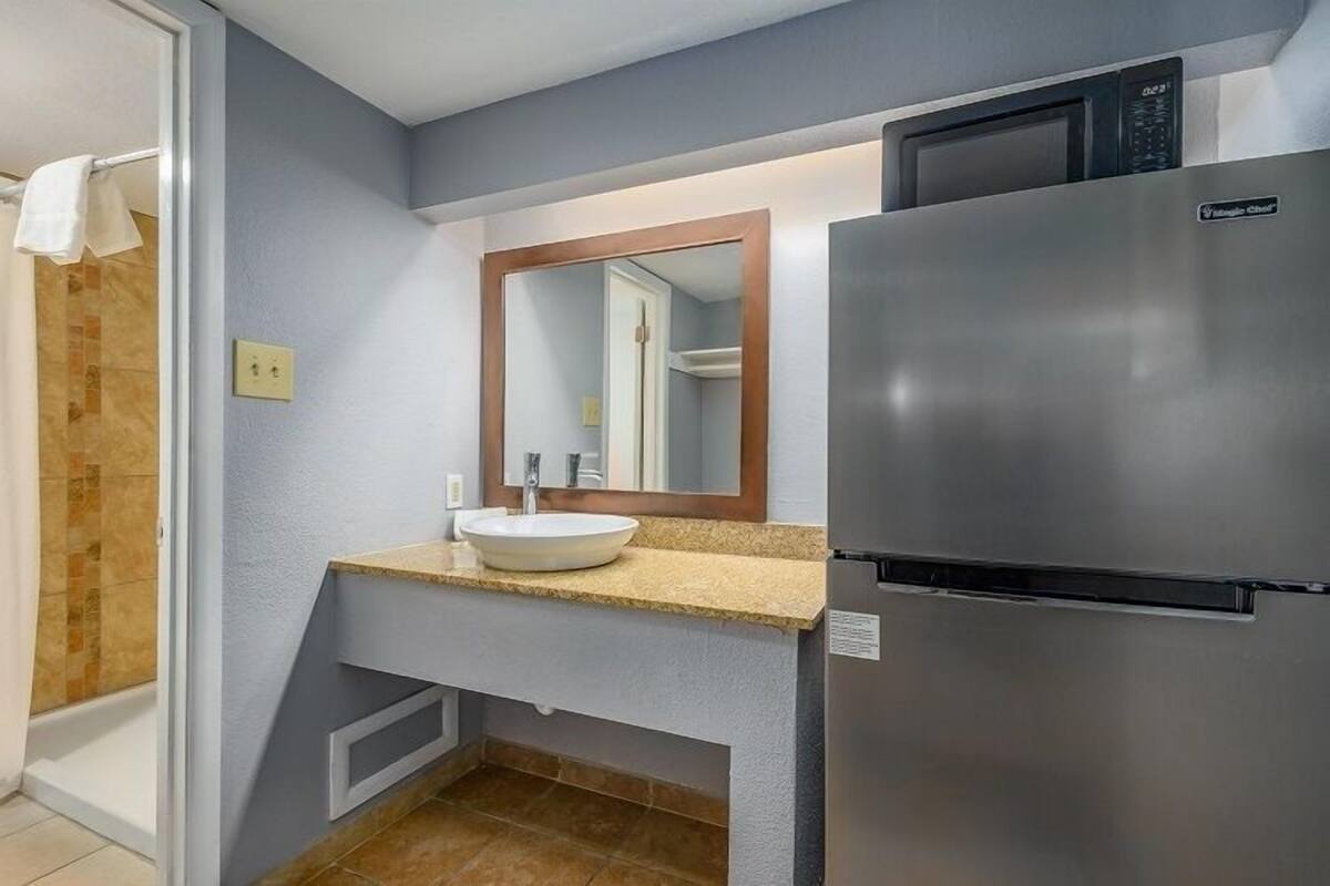 A compact bathroom with a built-in sink, a stainless steel refrigerator, and a microwave.