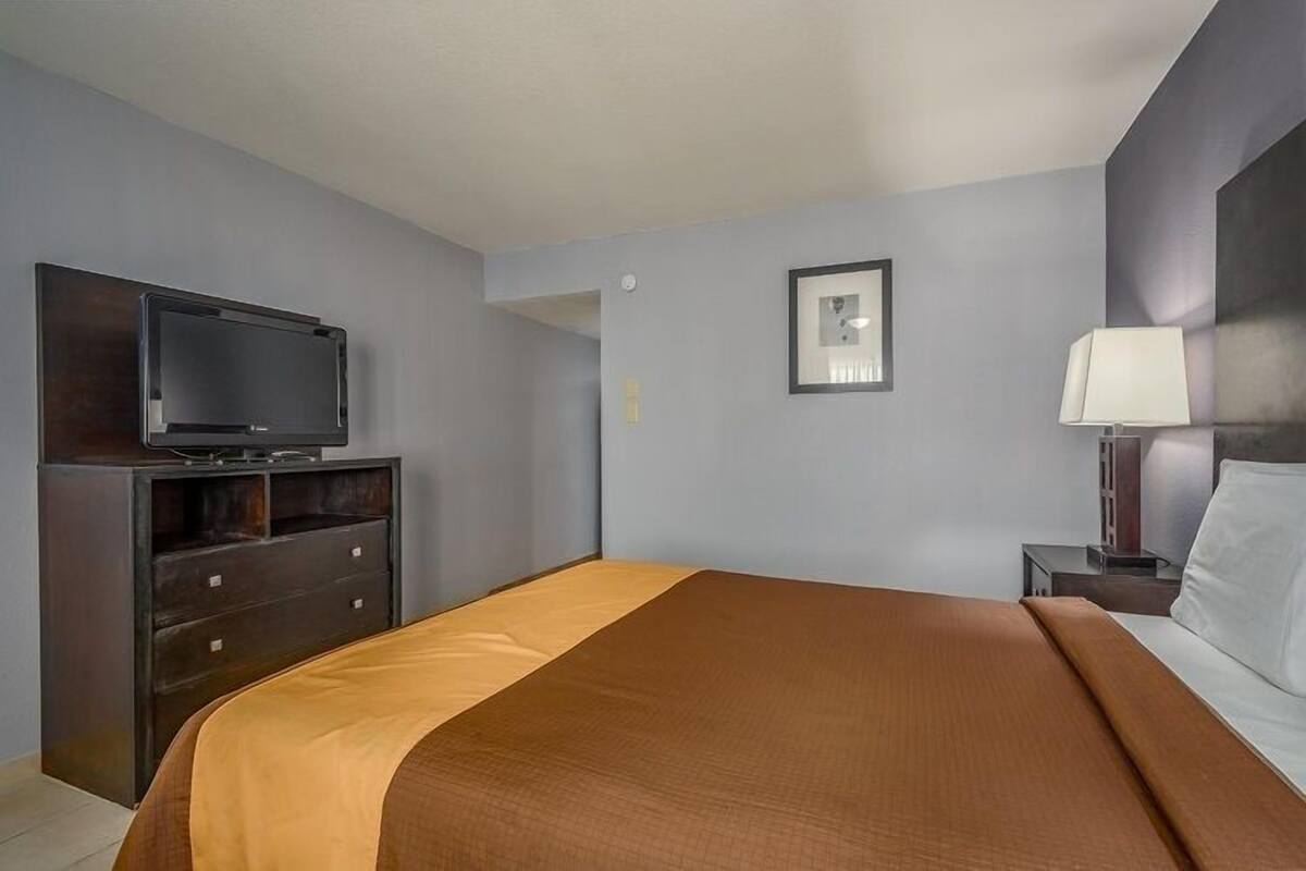 A hotel room with a bed, a TV on a dresser, a lamp, and a framed picture on the wall.