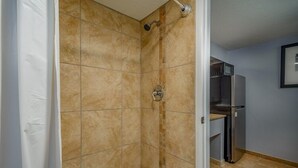 A bathroom with beige tiles, a shower, and a built-in kitchen area with a refrigerator and microwave. - Extend a Suites & RV Park (Albuquerque)
