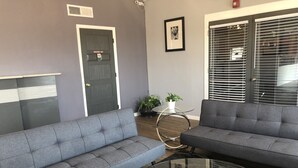 A modern living room with two grey sofas, a glass coffee table, a small white table with plants, and a door marked "Employees Only". - Extend a Suites & RV Park (Albuquerque)