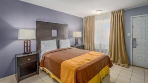 A hotel room with a bed, two bedside tables with lamps, a door, and a window with curtains. - Extend a Suites & RV Park (Albuquerque)