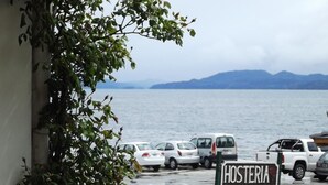 Ein Parkplatz mit einem Schild, auf dem 'Hosteria Las Amolitas' steht, vor einem Gewässer und Bergen.