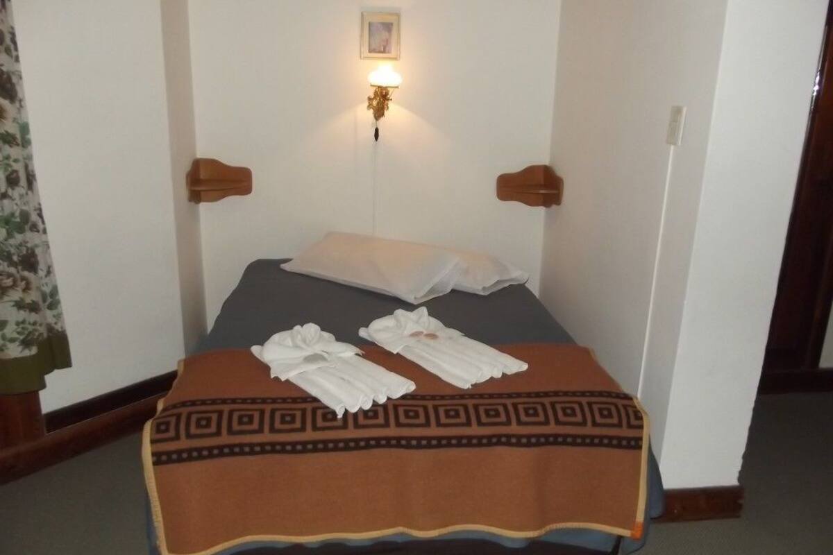 Una habitación de hotel con una cama, dos mesitas de noche, una lámpara de pared y un adorno decorativo en la pared.