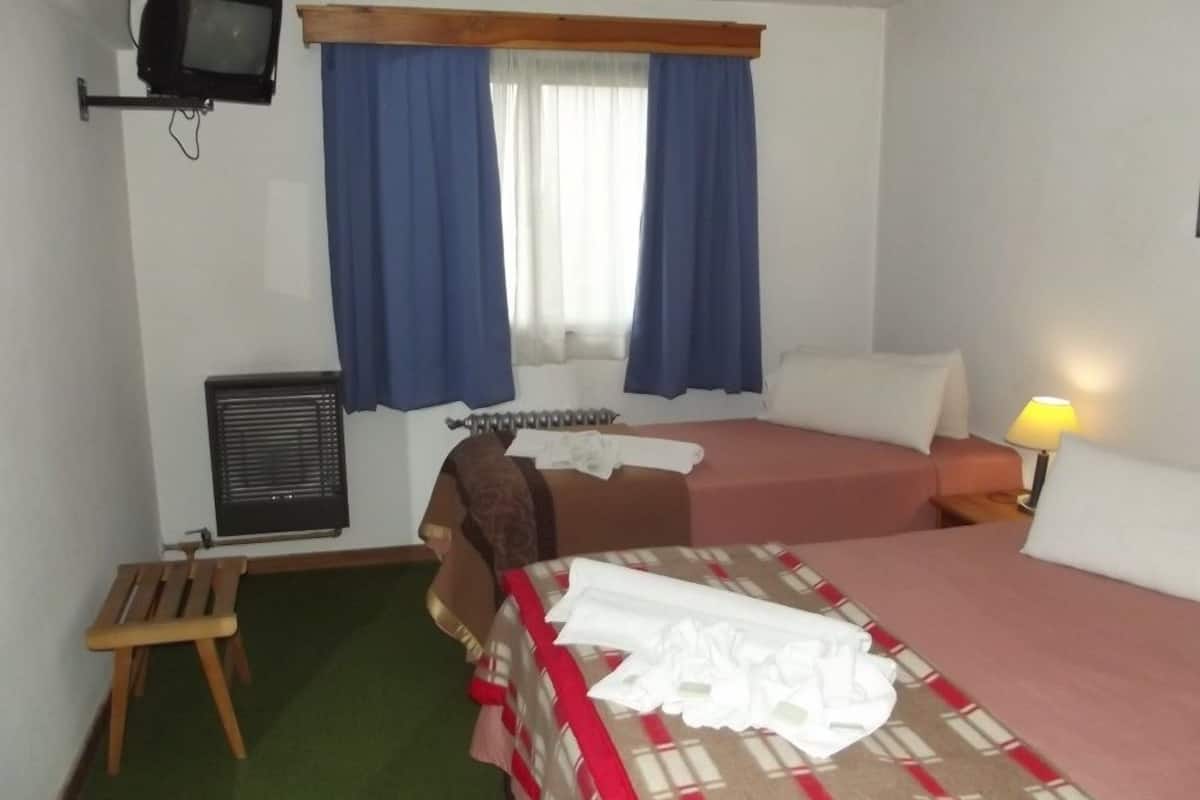 Habitación de hotel con dos camas, una mesita, televisor y ventana con cortinas.