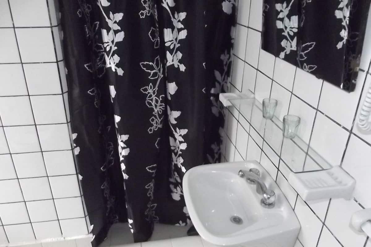 Un baño con lavamanos blanco, un espejo y cortina de ducha negra con estampado floral.