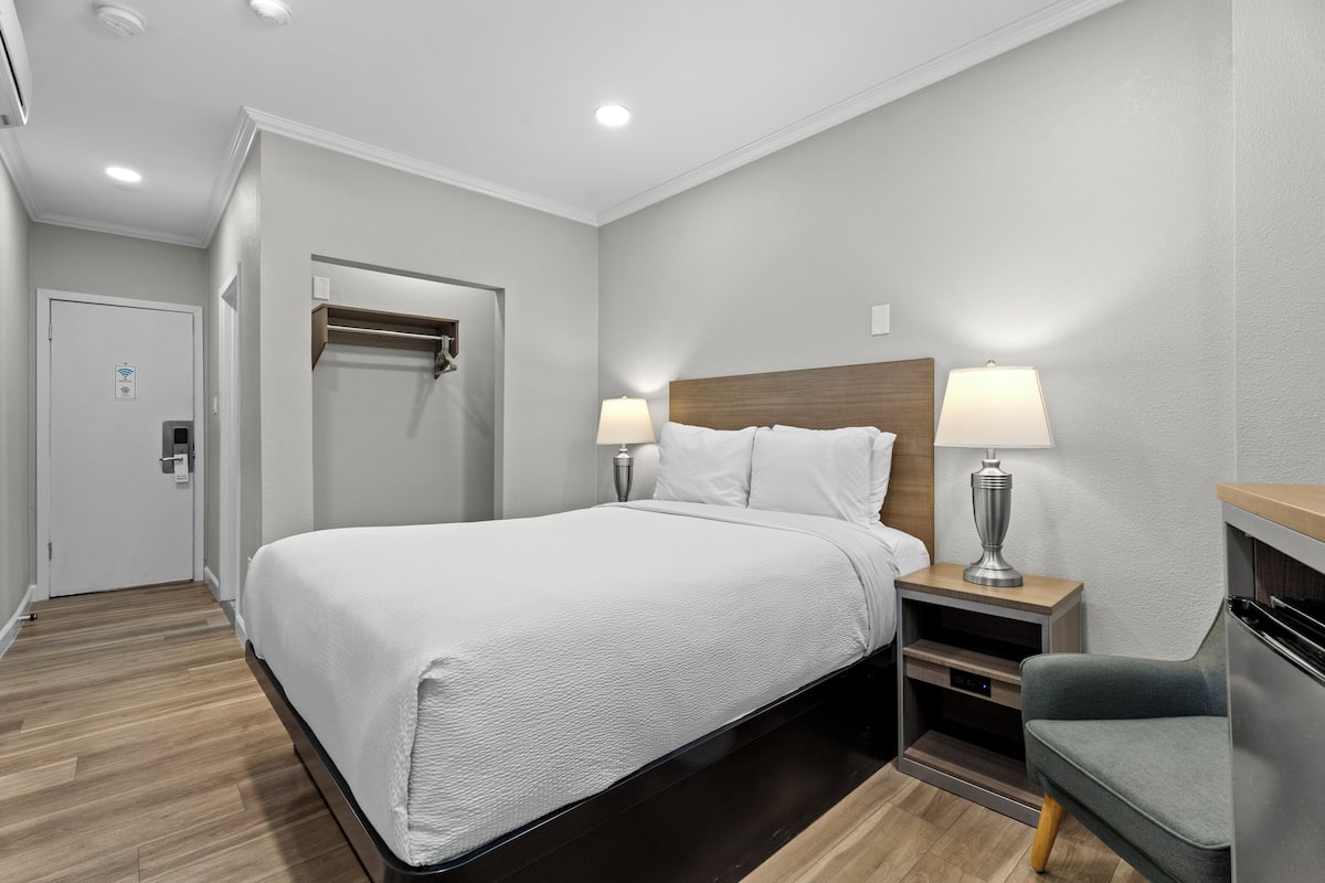 A hotel room with a large bed, two bedside tables with lamps, a wooden headboard, a small seating area, and a door with a towel rack.