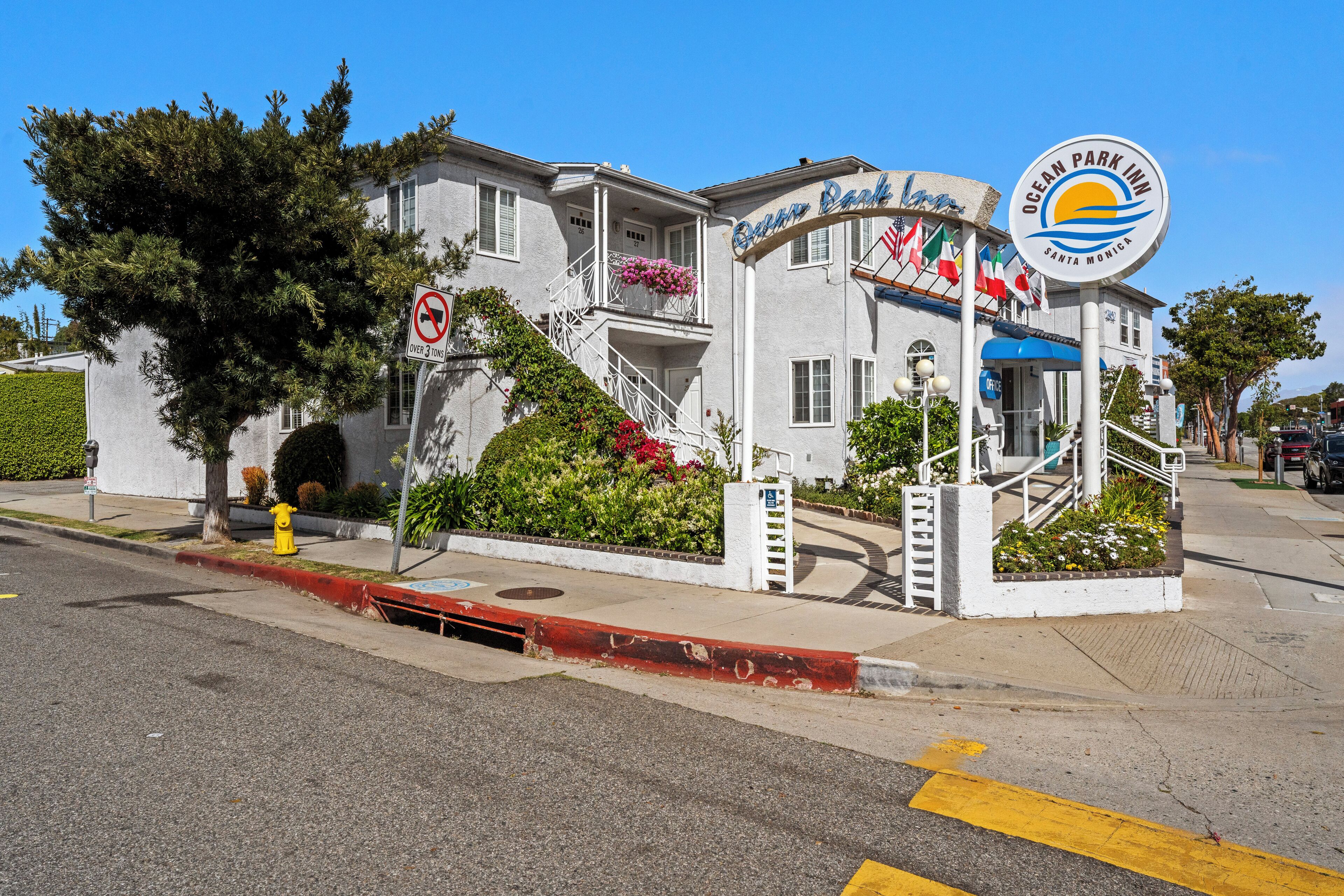 A building with a sign reading "Ocean Park Inn" and "Santa Monica." It features a staircase with railings, a fire hydrant, and a no left turn sign.