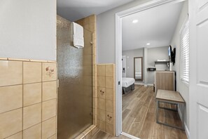 A modern bathroom with a shower, a toilet, and a sink. There is a bed in the adjacent room. - Ocean Park Inn (Santa Monica)