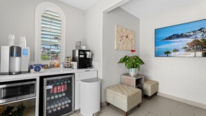 Una cocina moderna con cafetera integrada, un mini refrigerador con bebidas y una ventana con persianas.