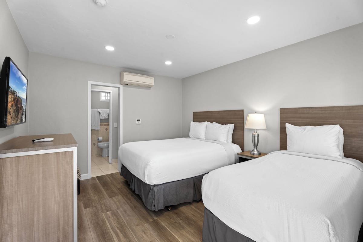 A hotel room with two beds, a desk, a TV, and an air conditioning unit.