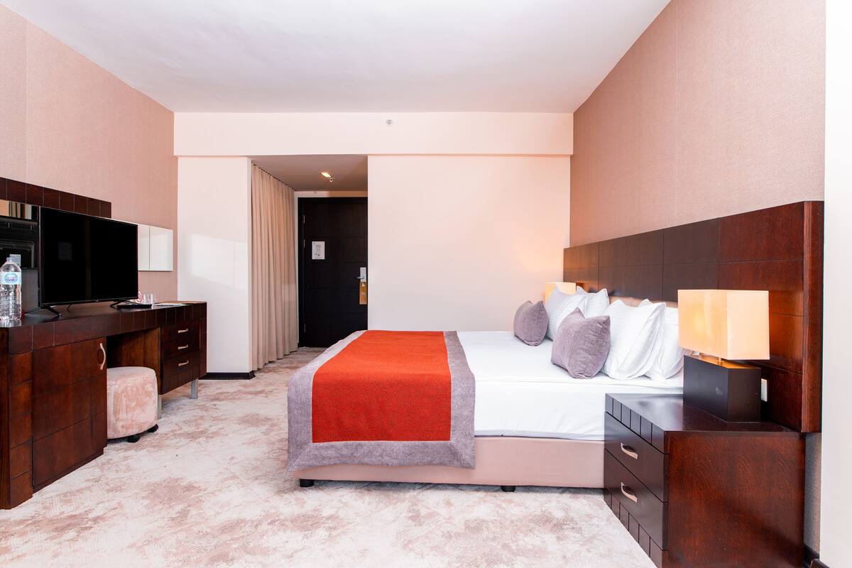 A hotel room with a bed, a desk, a television, and a bathroom visible through an open door.