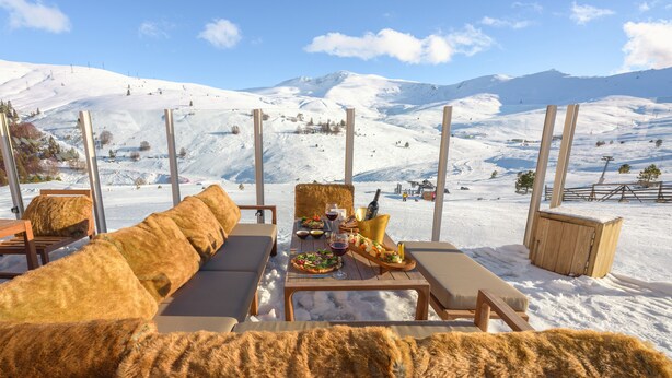 A snow-covered outdoor seating area with a wooden table, cushions, and a mountain view. - Monte Baia Uludag (Bursa)