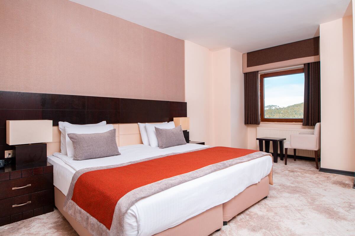 A hotel room with a large bed, bedside tables, a desk, and a window with curtains.