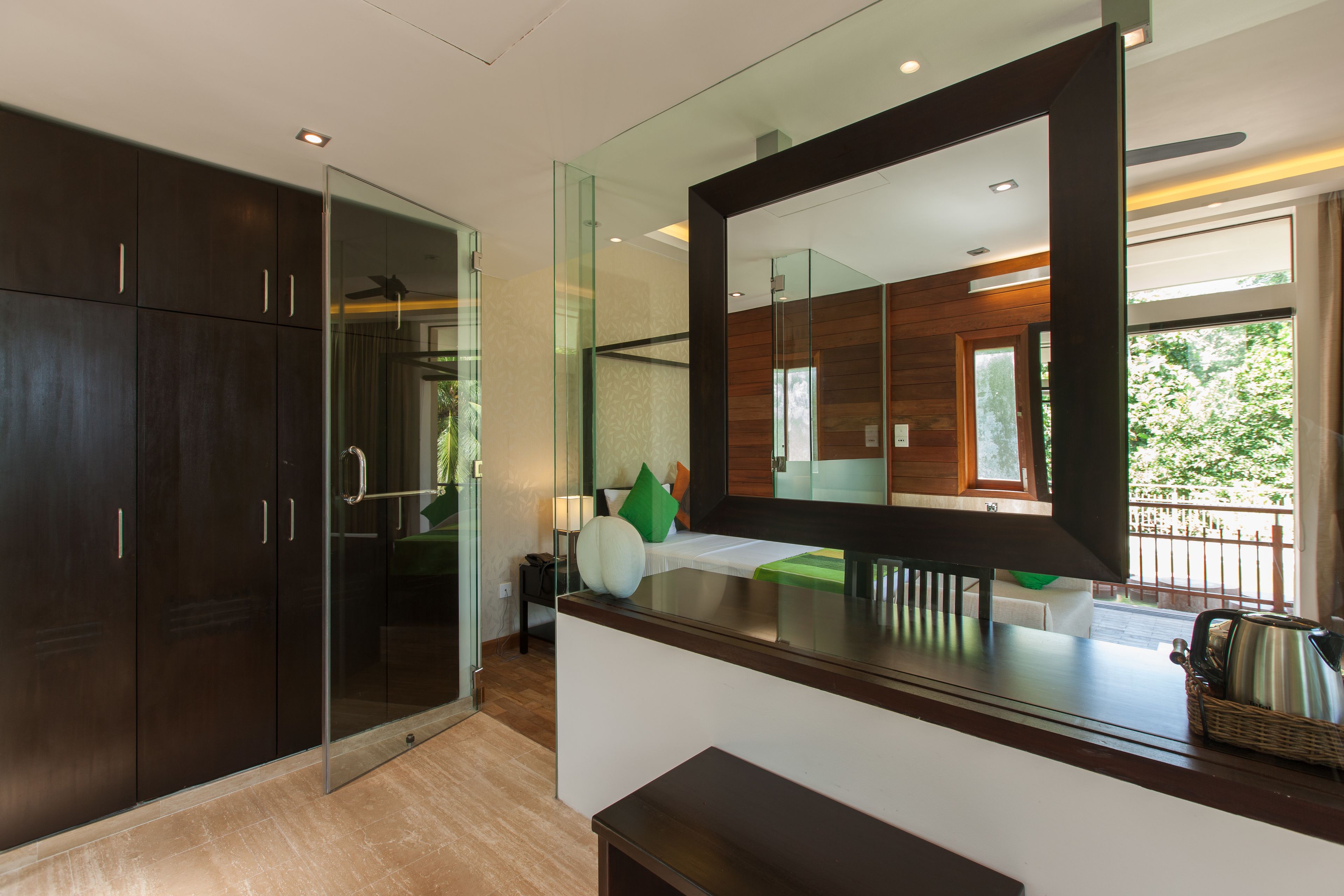 A modern bedroom with a large mirror, dark wood wardrobe, and a view of the outdoors.
