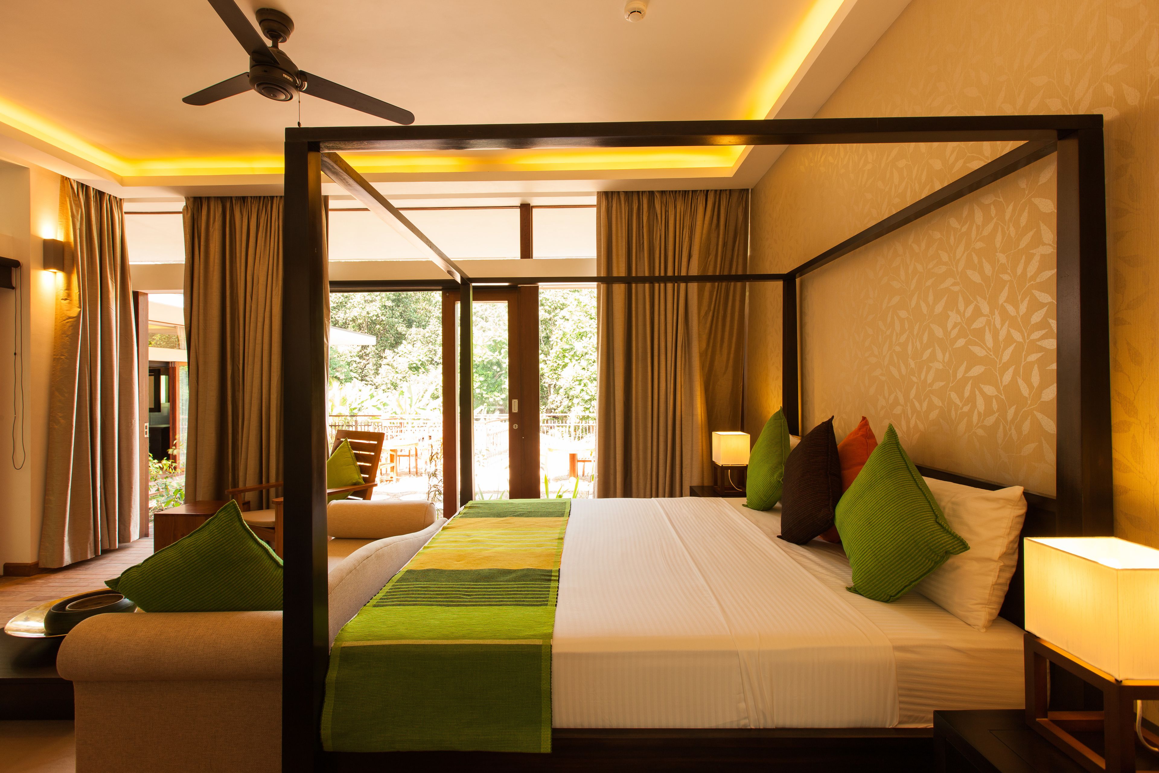 A four-poster bed with a green runner, a ceiling fan, and a view of the outdoors.