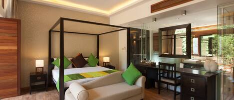 Una habitación de hotel moderna con una cama con dosel, un área de estar con sofá, un escritorio con espejo y un ventanal con vistas al exterior.