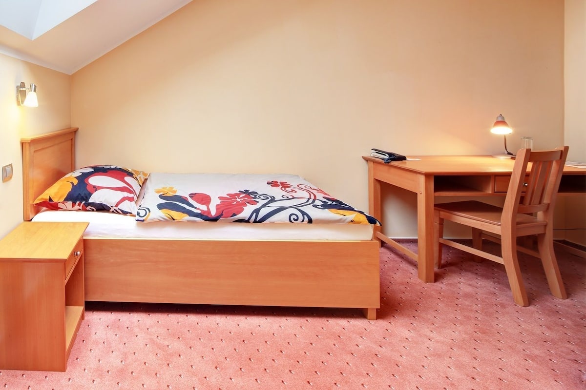 A small, cozy room with a bed, a desk, and a chair.