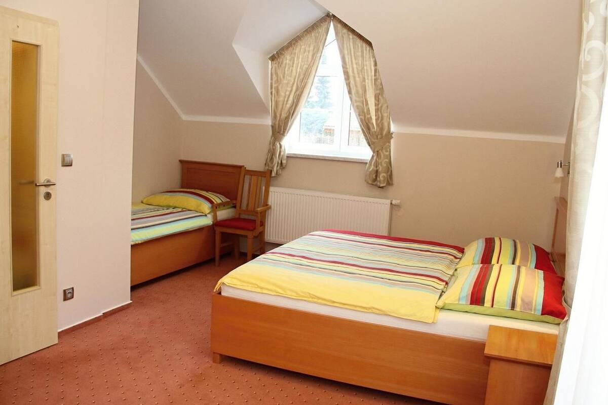 A bedroom with two single beds, a wooden chair, a radiator, and a window with curtains.