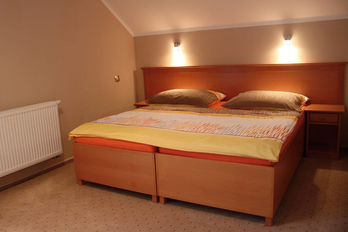 A bedroom with a wooden bed, two bedside tables, and a wall-mounted light fixture.