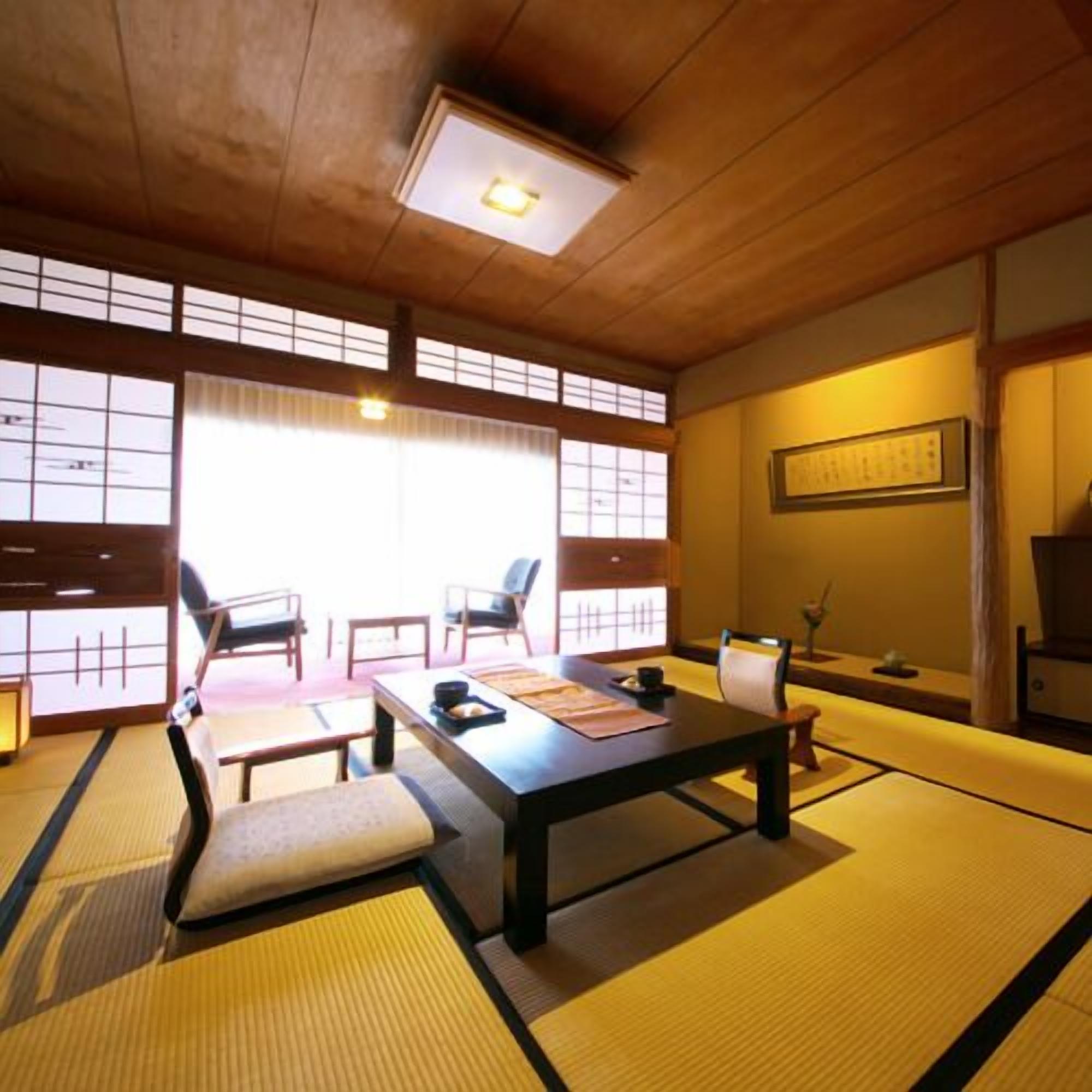 Ein traditioneller japanischer Raum mit Tatami-Böden, einem niedrigen Tisch, Stühlen und Schiebetüren.