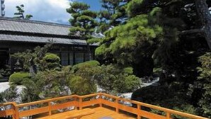 A wooden deck with tatami mats and cushions, surrounded by trees and a traditional building. - Ibusuki Shusuien (Ibusuki)