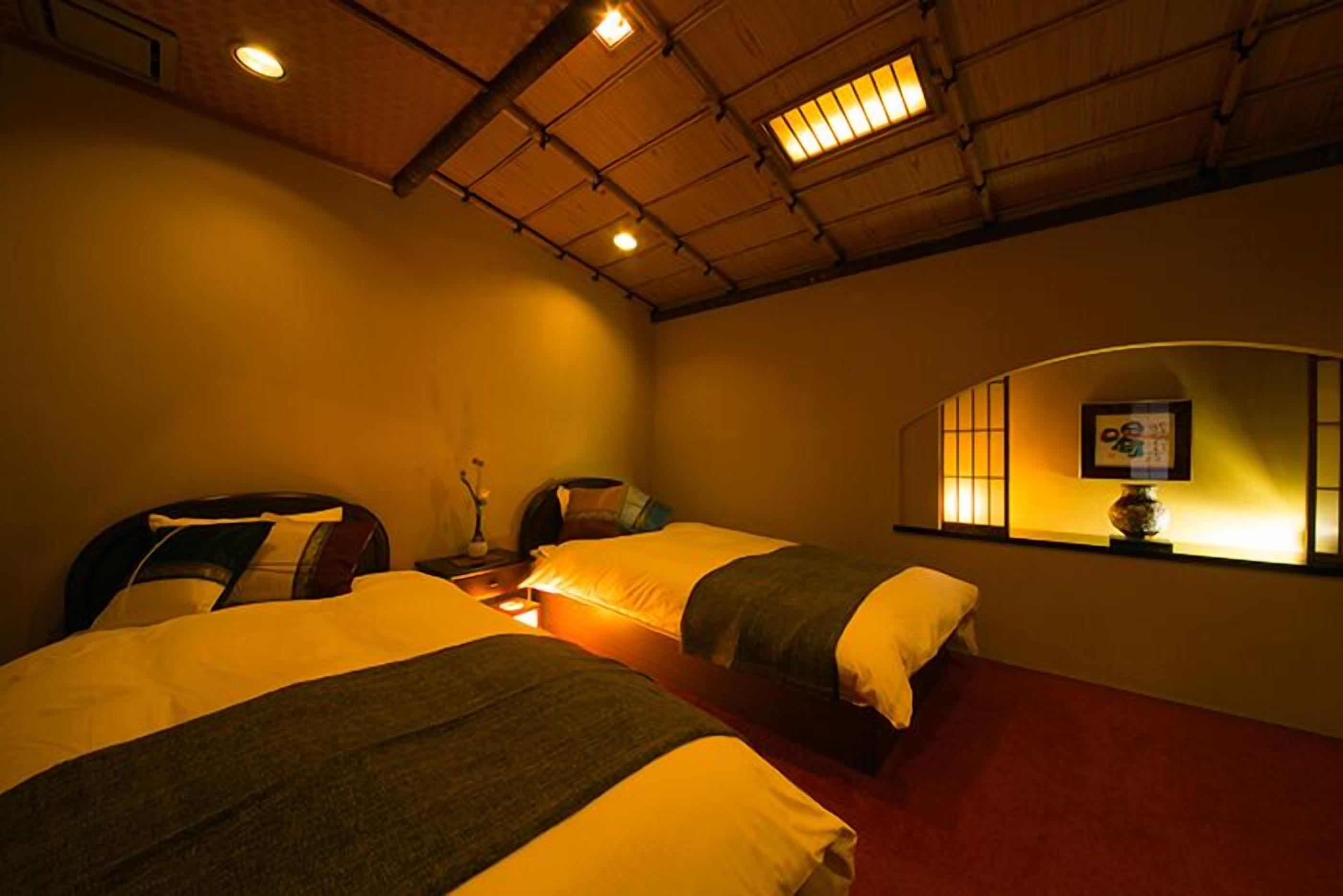 A hotel room with two beds, a wooden ceiling, and a wall-mounted lamp.