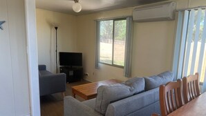 En stue med sofa, fjernsyn på et stativ og et vindue med gardiner.