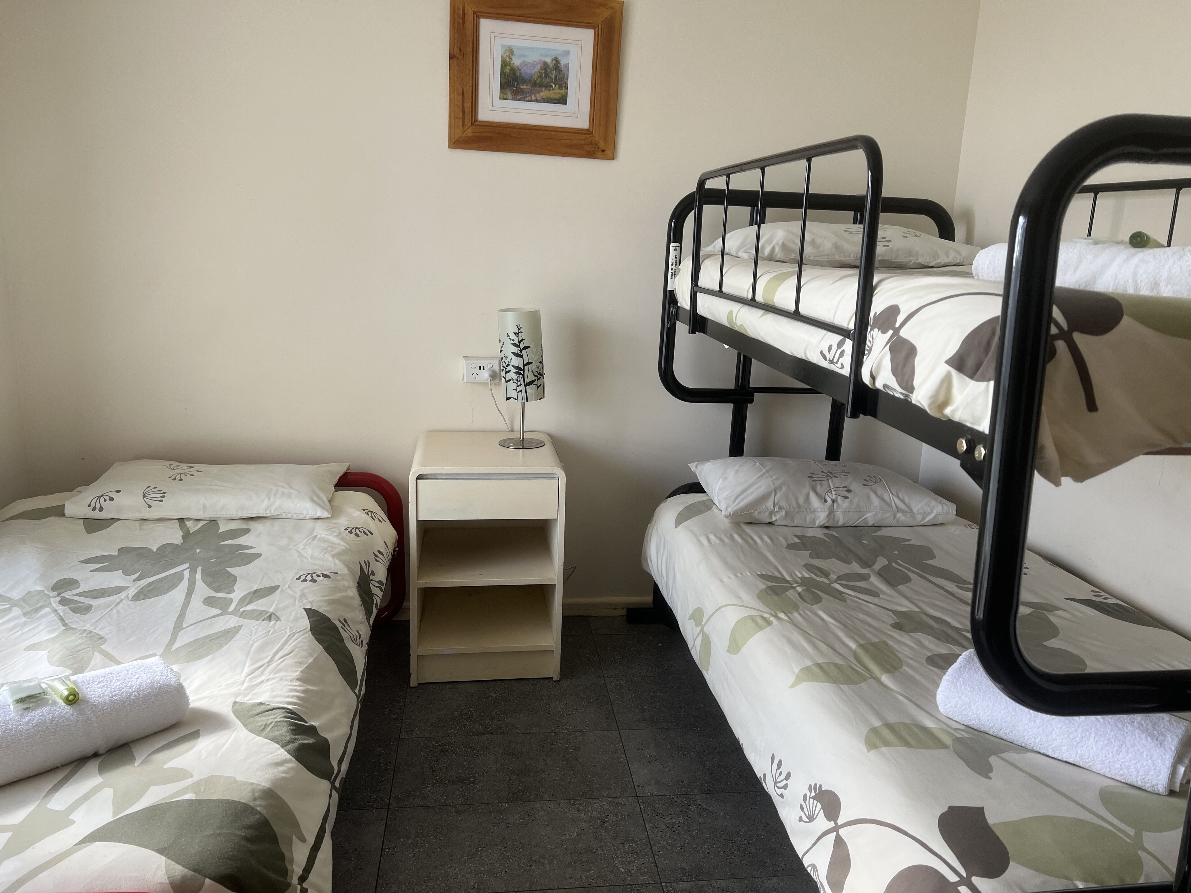 A room with two bunk beds, a bedside table with a lamp, and a framed picture on the wall.
