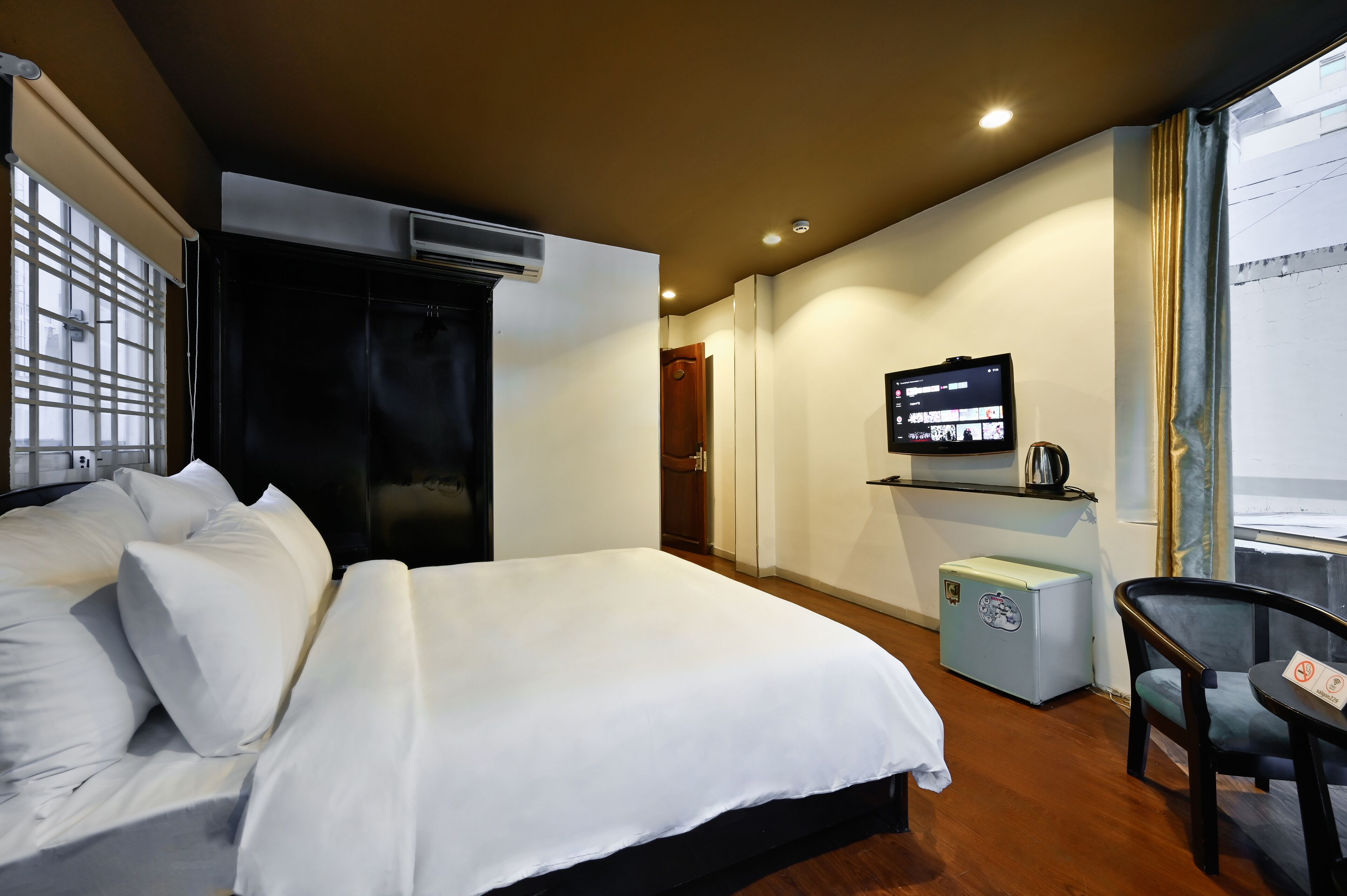 A hotel room with a bed, a TV, a small fridge, and a chair.