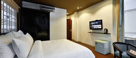 A hotel room with a bed, a TV, a small fridge, and a chair.